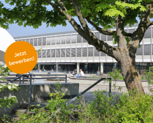 Blick auf das Gebäude 1 und den sommerlichen Campus. Im Vordergrund ist ein Teil einer grünen Baumes zu sehen. Links ist ein orangener Kreis, in dem 'Jetzt bewerben!' steht. 